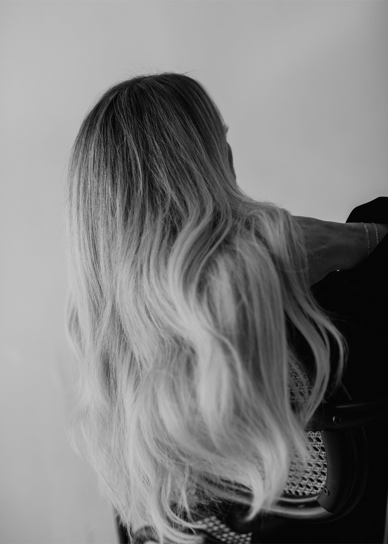 Black and white image of long, wavy blonde Vera Hair Co micro-tied wefts draped over chair, showcasing extension texture and fullness