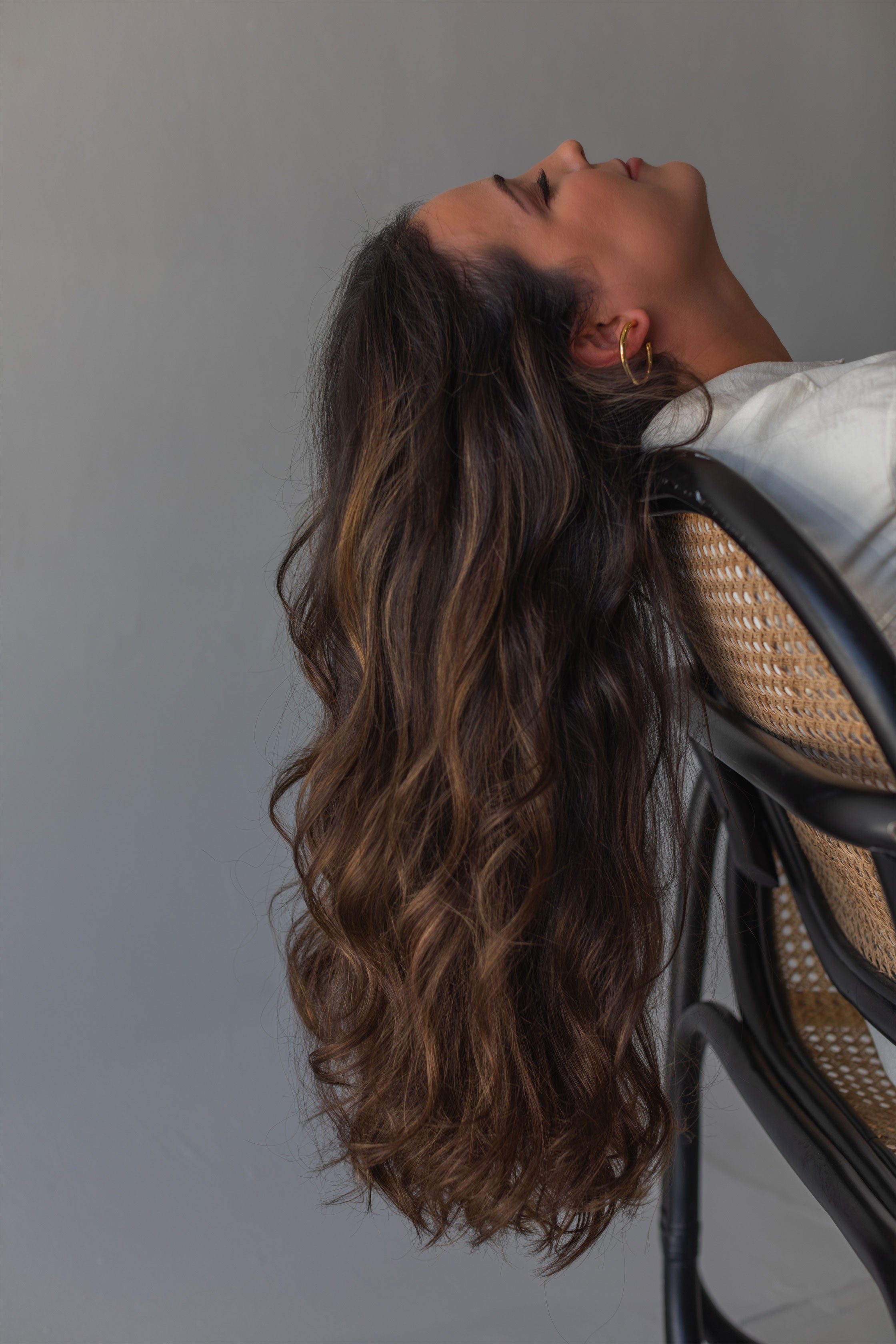 Brunette model with wavy Vera Hair Co micro-tied wefts draped over chair, showcasing healthy extension texture and at-home care results